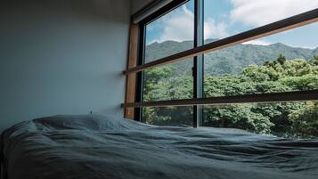 A bed in a room with a large window overlooking a mountainous landscape.