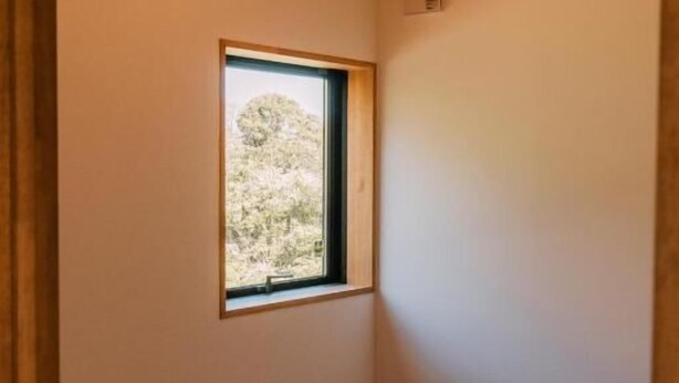 A room with a slatted bench, a window with a view of trees, and a light fixture on the ceiling.
