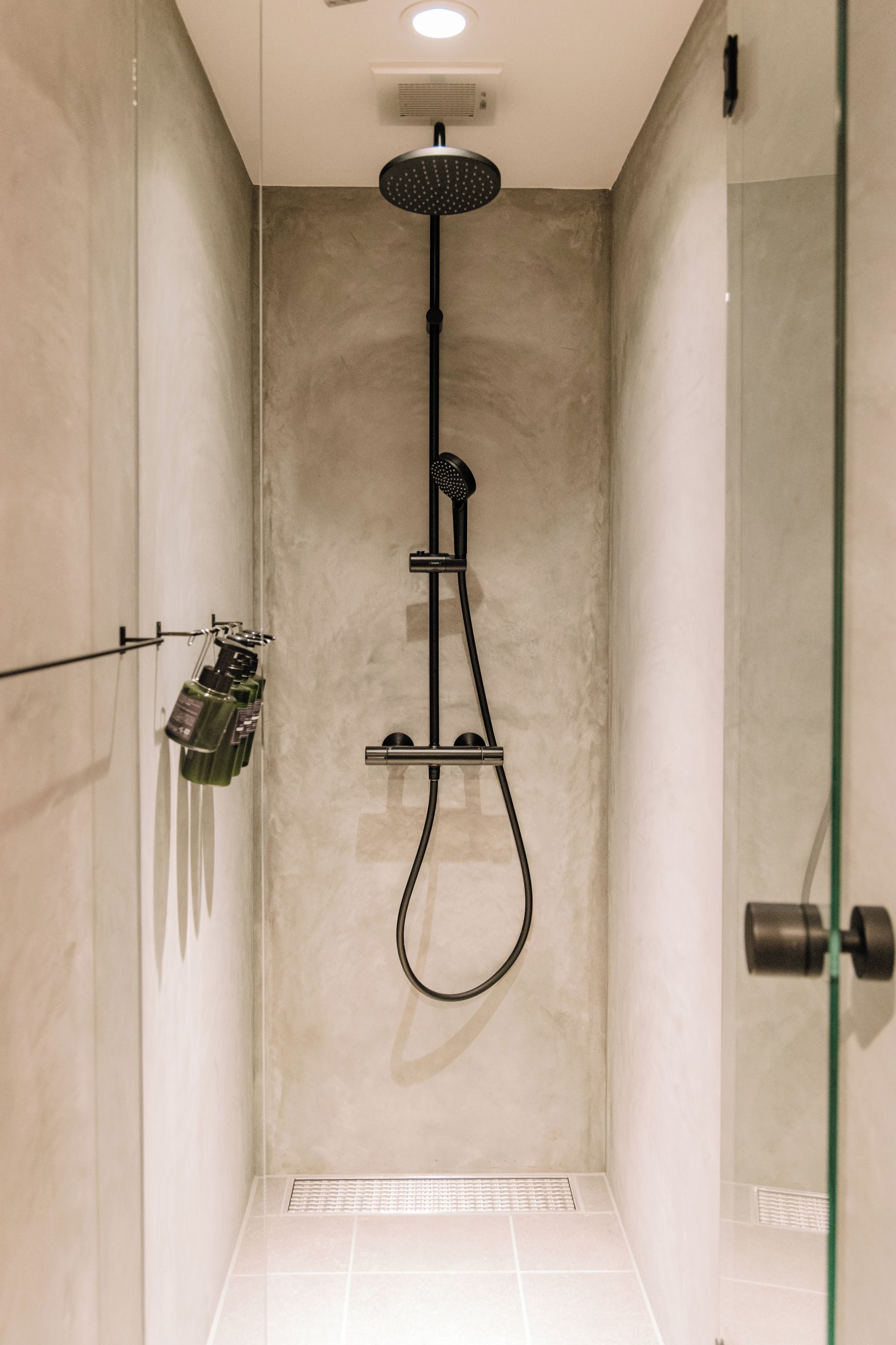 Eine moderne Dusche mit Handbrause und Deckenbrause, einer Glasduschtür sowie einem gefliesten Boden.