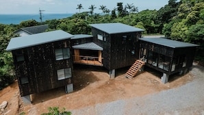 A modern, multi-story building with a flat roof, surrounded by dense tropical vegetation and a view of the ocean.