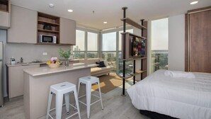 Ein modernes Hotelzimmer mit Küchenzeile, einem großen Bett, einer Sitzecke mit Blick und einem Balkon.