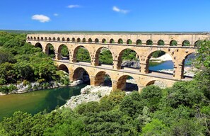 Eine Steinbrücke mit mehreren Bögen über einem Fluss, umgeben von viel Grün.