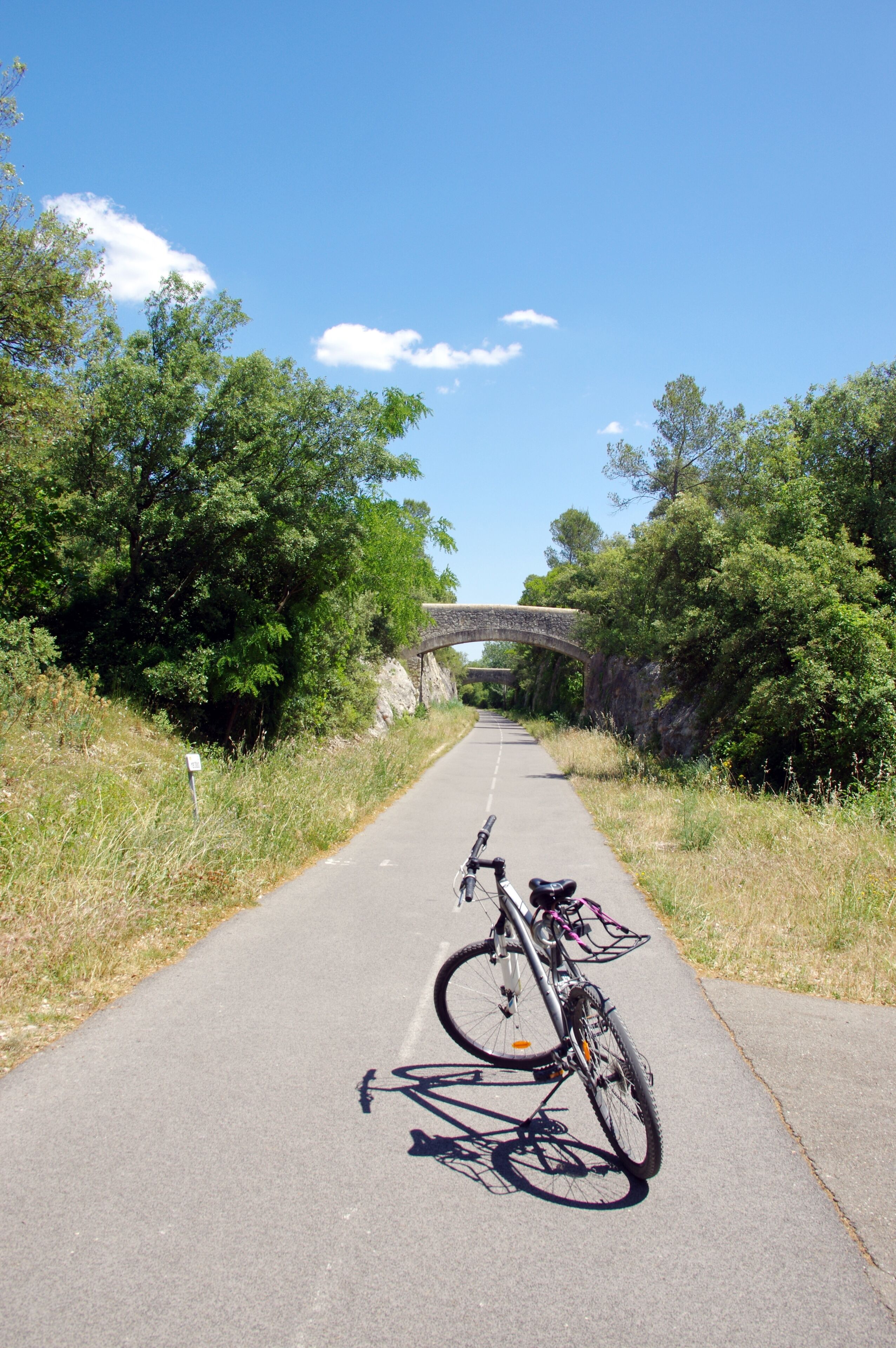 A paved path with a bicycle, a stone bridge, and lush greenery.