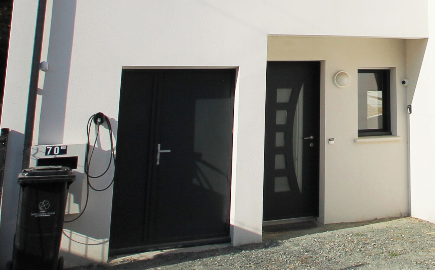A building with two black doors, a small window, and a recycling bin.
