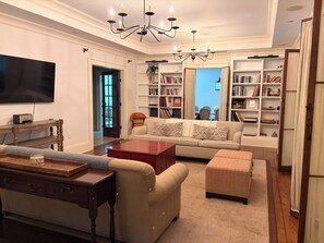 A living room with a sofa, ottoman, coffee table, bookshelf, and a flat-screen TV. - Hudson Valley Retreat! New Paltz + Kingston (Ulster Park)