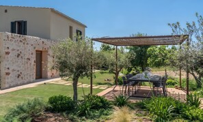 Un patio con mobiliario exterior, una pérgola y un jardín con diversas plantas.