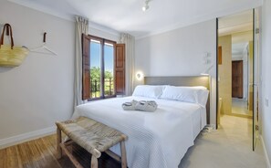 Un dormitorio con cama, banca y vistas al verdor exterior.