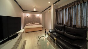 Um quarto moderno com uma cama, uma televisão, uma mesa de centro de vidro e um sofá de couro.