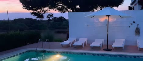 Piscina com cadeiras de descanso e uma parede branca ao fundo.
