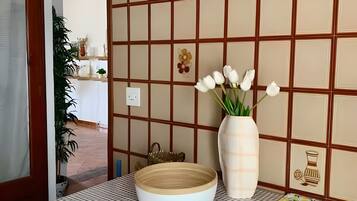 A dining area with a checkered tablecloth, a vase with white flowers, and a decorative wall with a grid pattern and floral motifs.
