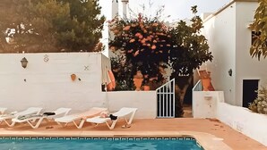 A swimming pool with lounge chairs, a white building, and a tree with red flowers. - Country House Near Ciutadella with Private Pool, Shared Terrace, and Wi-Fi (Ciutadella)