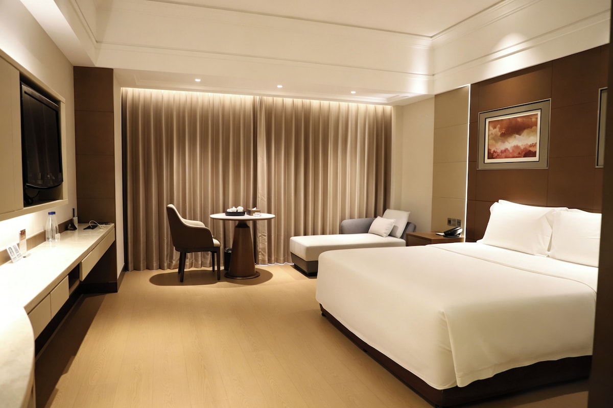 Une chambre d’hôtel équipée d’un lit, d’un bureau, d’une chaise, d’une petite table et d’un téléviseur.
