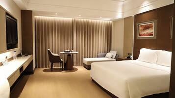 A hotel room with a bed, a desk, a chair, a small table, and a television.