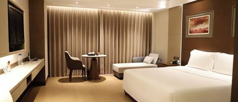 Ein Hotelzimmer mit einem Bett, einem Schreibtisch, einem Sessel, einem kleinen Tisch und einem Fernseher.