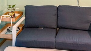 Een kamer met een bank, een kleine tafel met een plant en een wandplank met een camera.