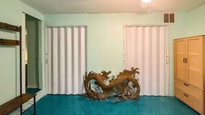 Een kamer met smaragdgroene vloerbedekking, een houten bank, een decoratieve draak sculptuur en een garderobe.