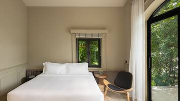 Un dormitorio con una cama grande, una silla, una mesita y un ventanal con vistas a zonas verdes.
