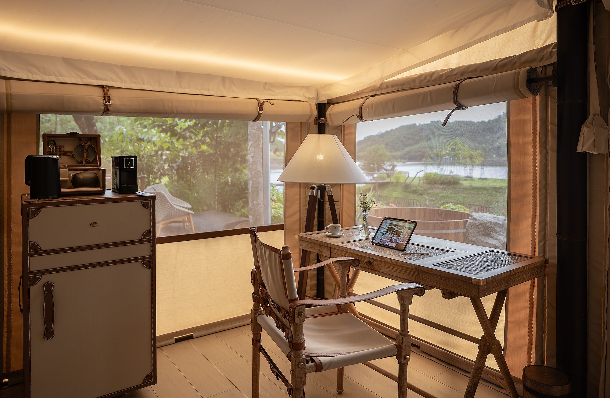 Una habitación acogedora con un escritorio de madera, una computadora portátil, una lámpara y vista a un lago.