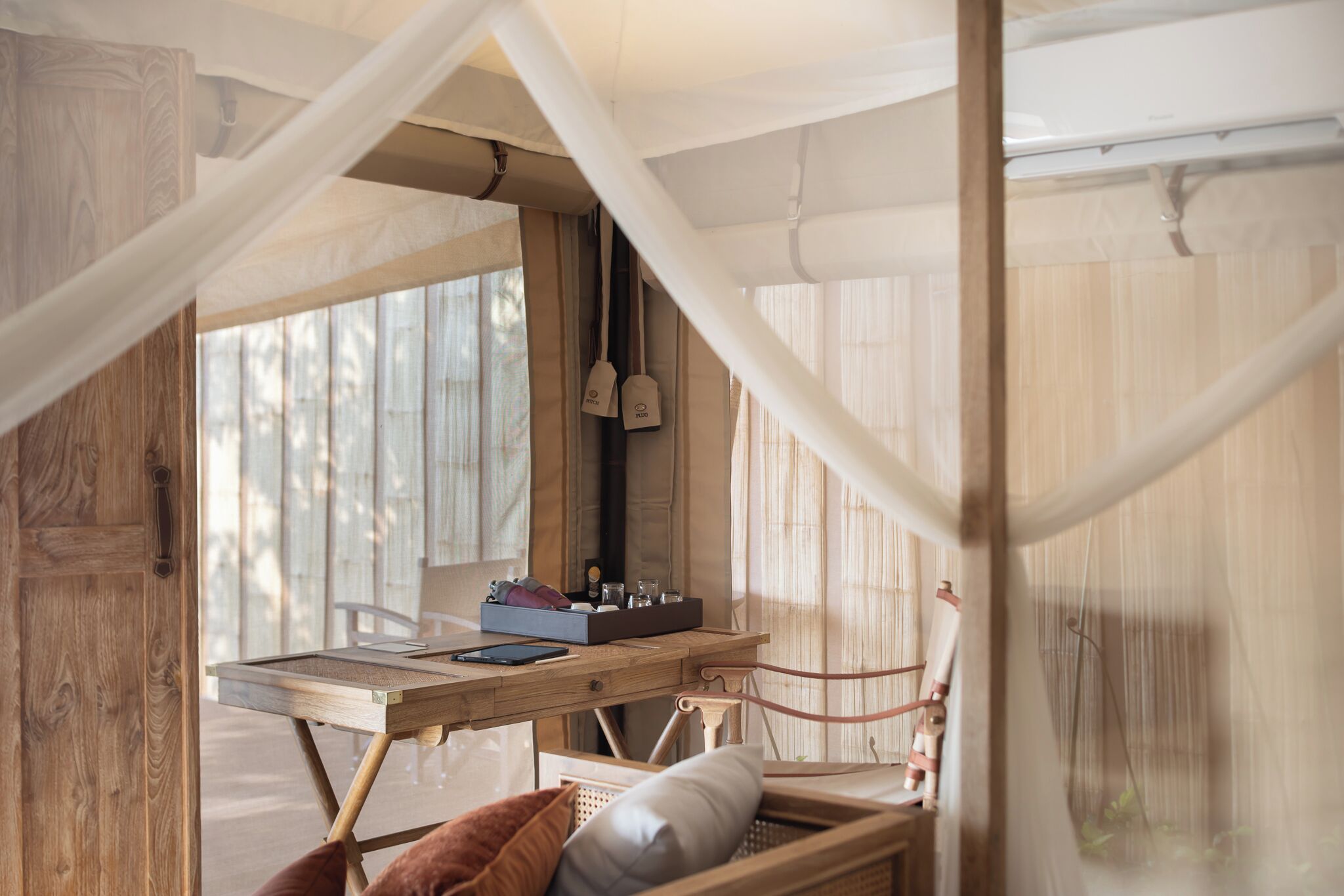 A wooden bed with a canopy, a small table with a box and a tablet, and a window with curtains.