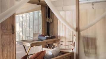 Una cama de madera con dosel, una mesita con una caja y una tableta, y una ventana con cortinas.