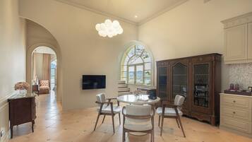 A dining area with a round table, chairs, a chandelier, and a view through a window.