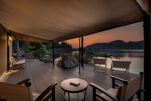 Un espacio de estar techado al aire libre con vista a un lago y colinas al atardecer.