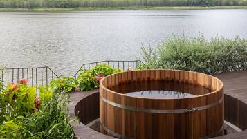 Tinaco de madera sobre un muelle de madera junto a un lago, con barandilla de metal y vegetación.