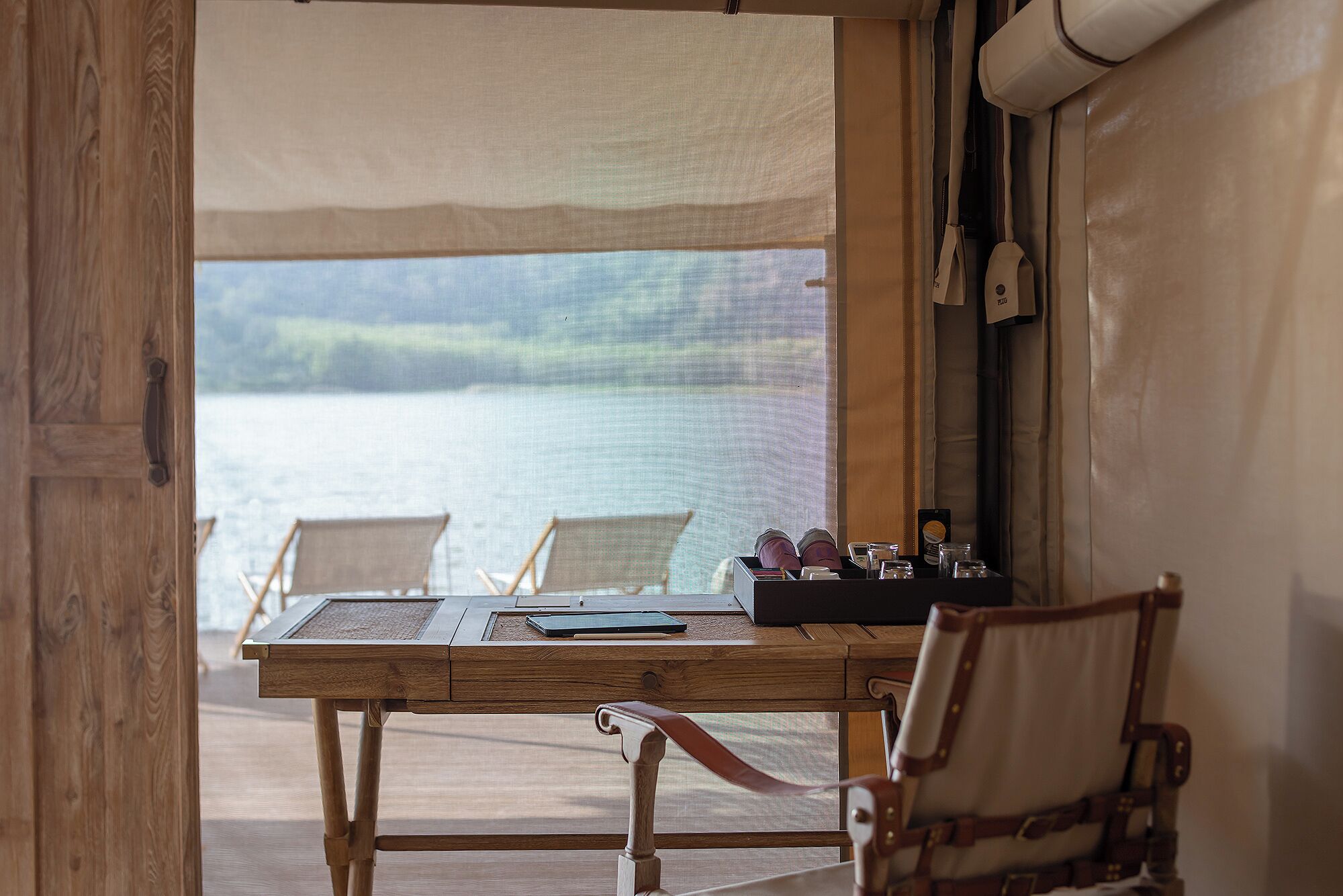 A wooden table with a view of a body of water, two chairs, and a small table with items on it.