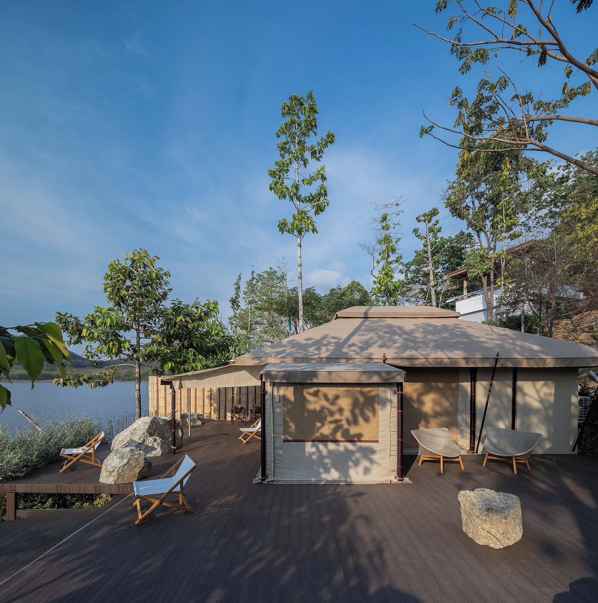 A wooden deck with lounge chairs and a covered seating area overlooking a body of water.