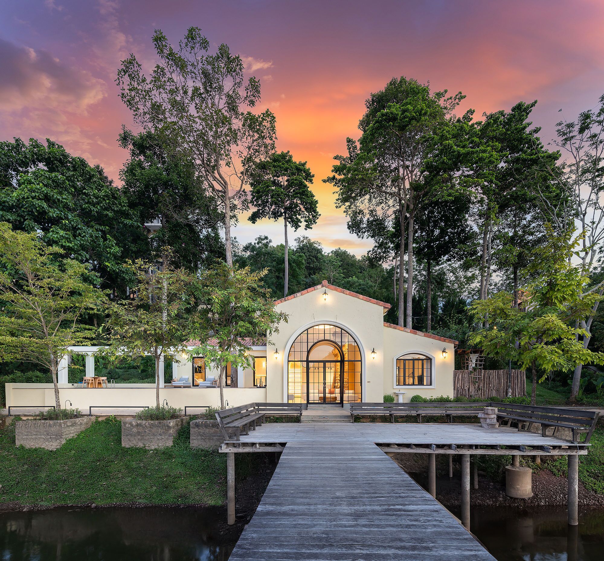 A house with a large arched entrance, a wooden deck, and a pond in front.