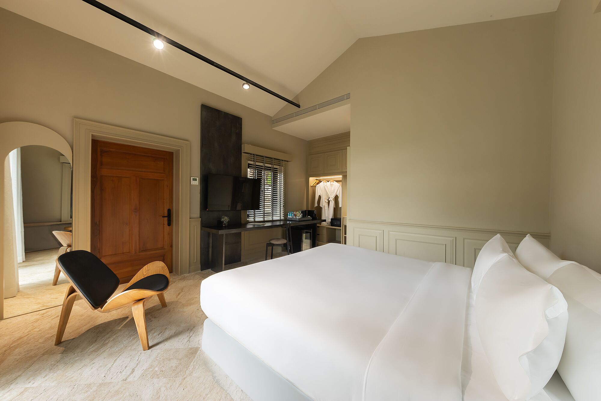 Una habitación de hotel con una cama grande, una silla de madera, un escritorio con televisor de pantalla plana y un vestidor.
