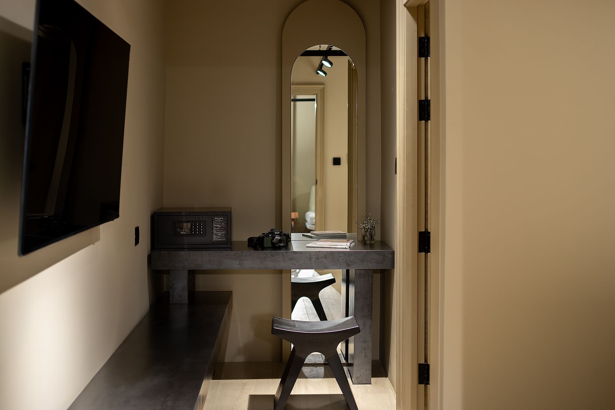 A hallway with a dark wooden bench, a small table with a microwave, and a mirror reflecting a door and a light fixture.