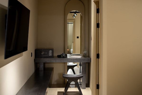 Un couloir avec un banc en bois sombre, une petite table sur laquelle se trouve un four à micro-ondes, et un miroir qui reflète une porte et un luminaire.