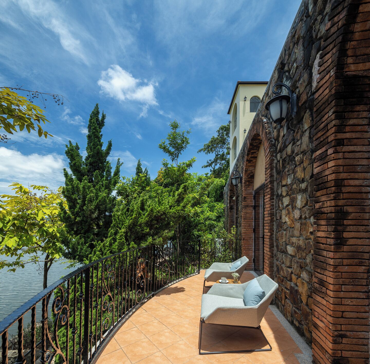 A balcony with two lounge chairs, a brick wall, and a view of the water.