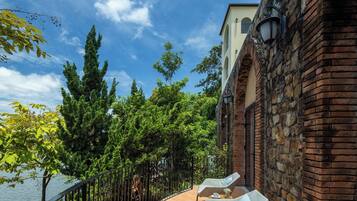 A balcony with two lounge chairs, a brick wall, and a view of the water.
