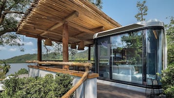Ein moderner Außenbereich mit Sitzgelegenheit, einer Glasverkleidung, einem Holzterrassenboden und Blick auf einen See.