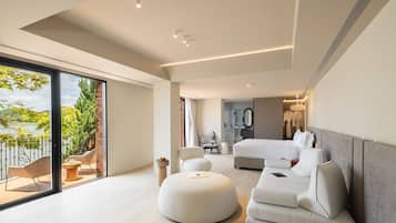 A modern bedroom with a large bed, a seating area with ottomans, and a view of a lake through a glass door.