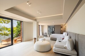 Un dormitorio moderno con una cama grande, un área de descanso con otomanas y vista a un lago a través de una puerta de vidrio.