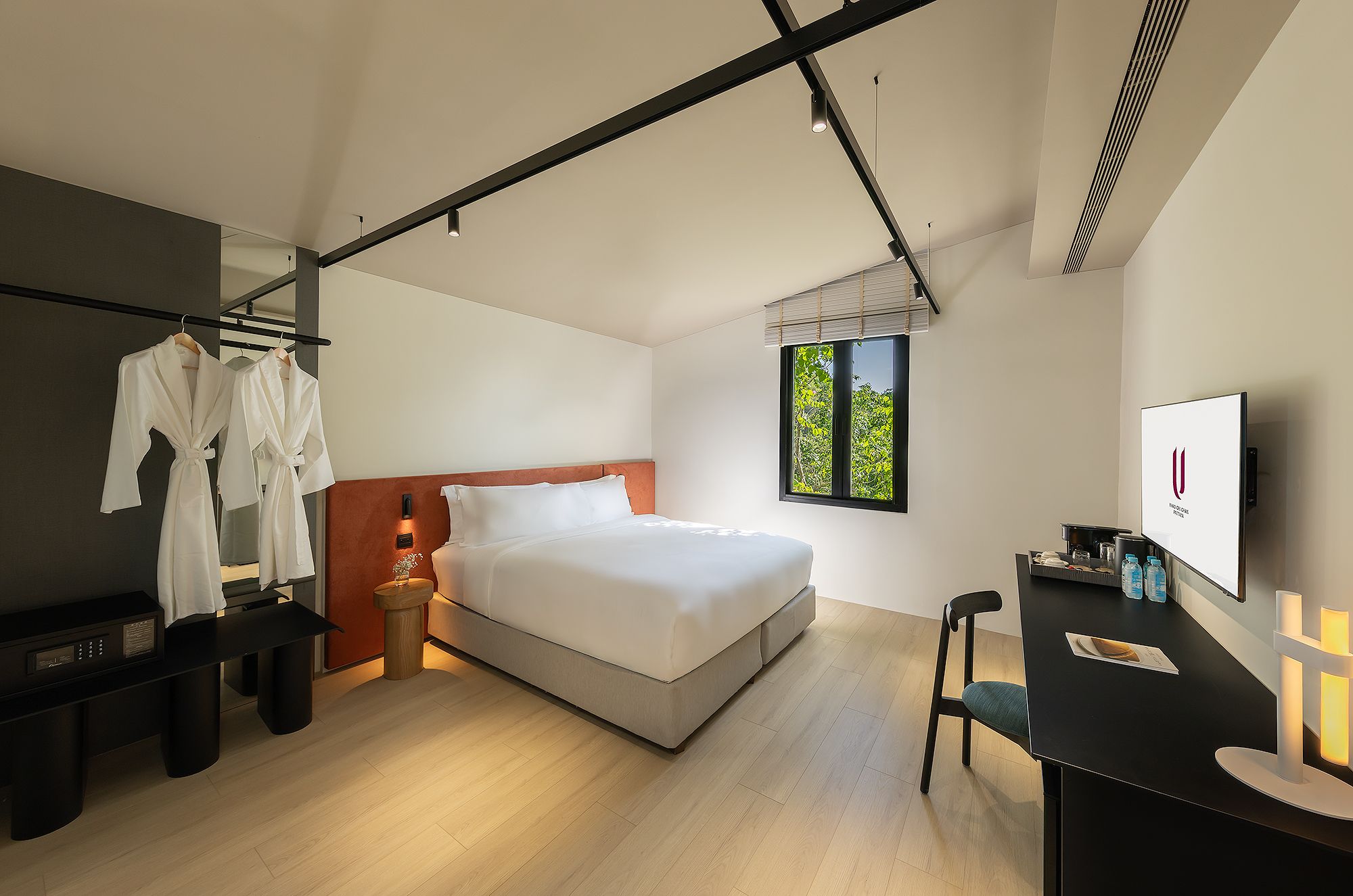A modern hotel room with a bed, a desk, a chair, a TV, and a window with a view of trees.