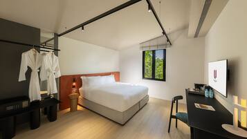 A modern hotel room with a bed, a desk, a chair, a TV, and a window with a view of trees.