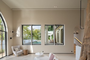 A modern interior with large windows, a white sofa, a round wooden table, and a staircase.