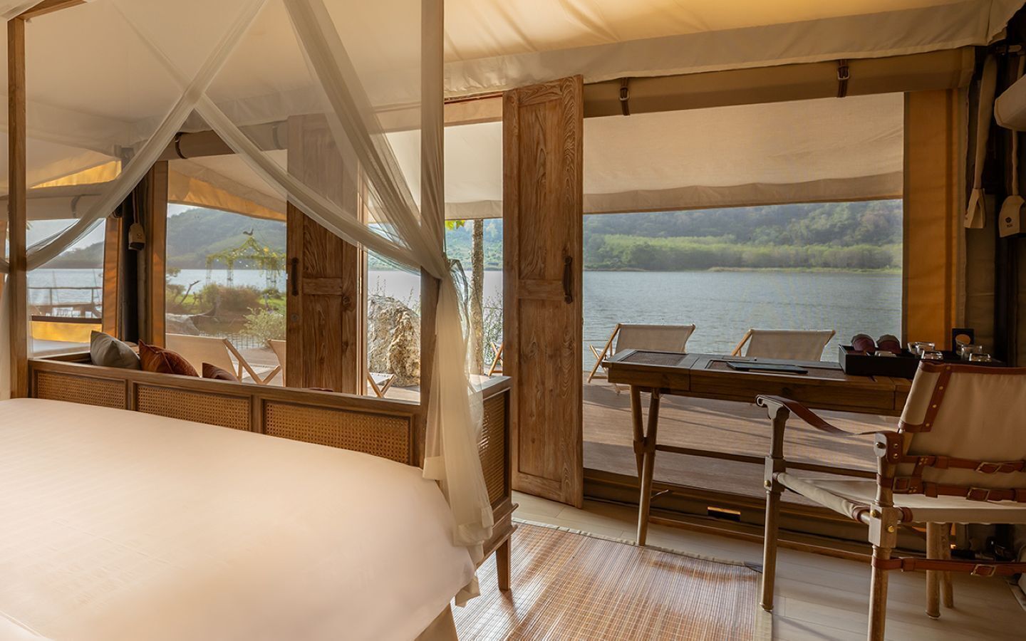 Una habitación con cama, mesa y sillas, y vista a un lago y un bosque.