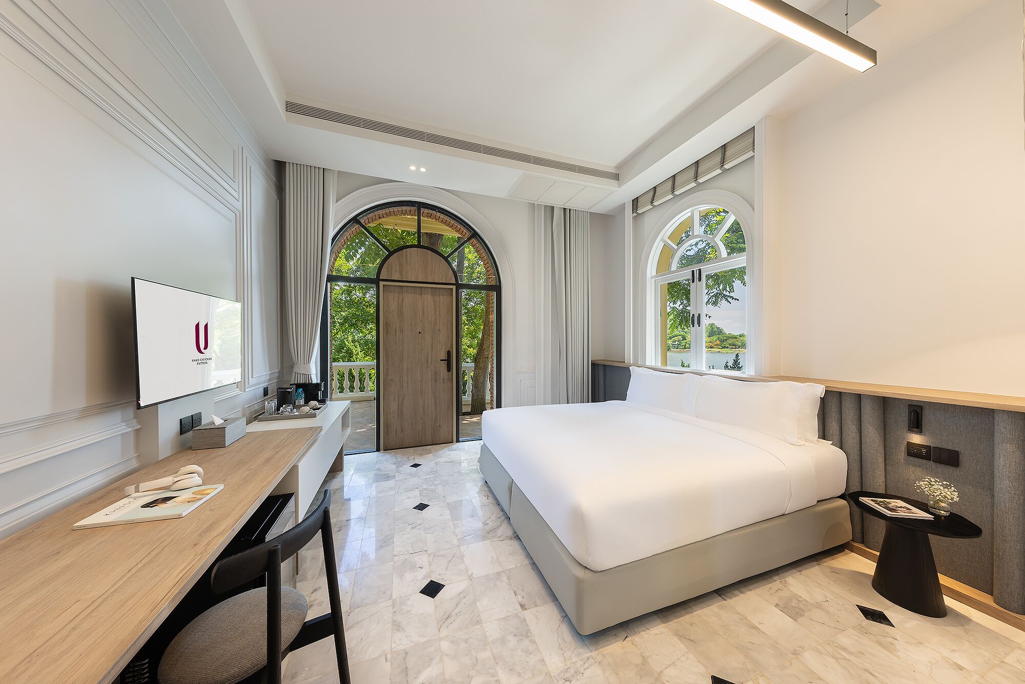 Habitación de hotel con cama, escritorio, televisión y vistas a zonas verdes.