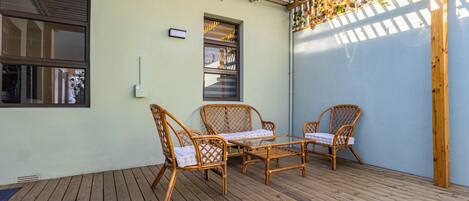 A covered patio with wicker furniture, a wooden deck, and a light-colored wall.