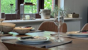 Ruokailutilassa on puinen pöytä, tuolit, riippuvalaisin ja ikkunasta avautuu näkymä vehreään maisemaan.