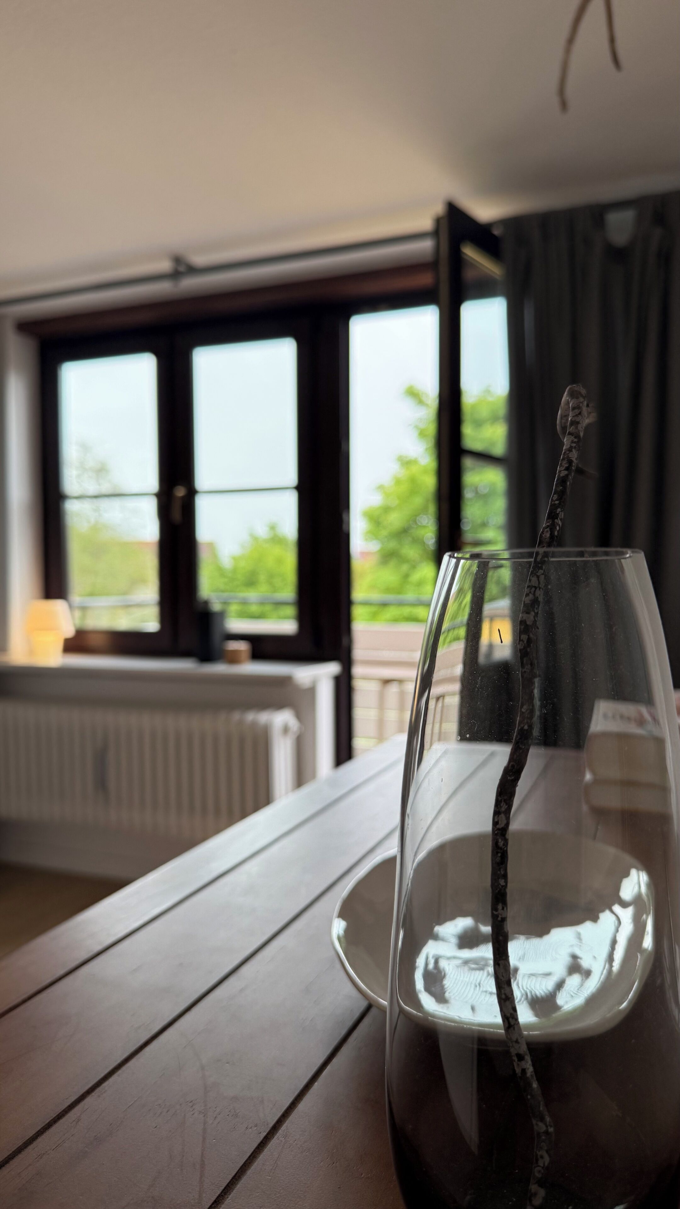 A glass of dark liquid on a wooden table with a view of a window and a radiator in the background.