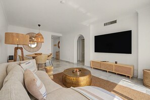 A spacious living room with a large flat-screen TV mounted on the wall, a comfortable sofa, a round coffee table, and a dining area with wicker furniture. - Apartment 'Vista Azul' with Sea View, Wi-Fi and Air Conditioning (La Herradura)