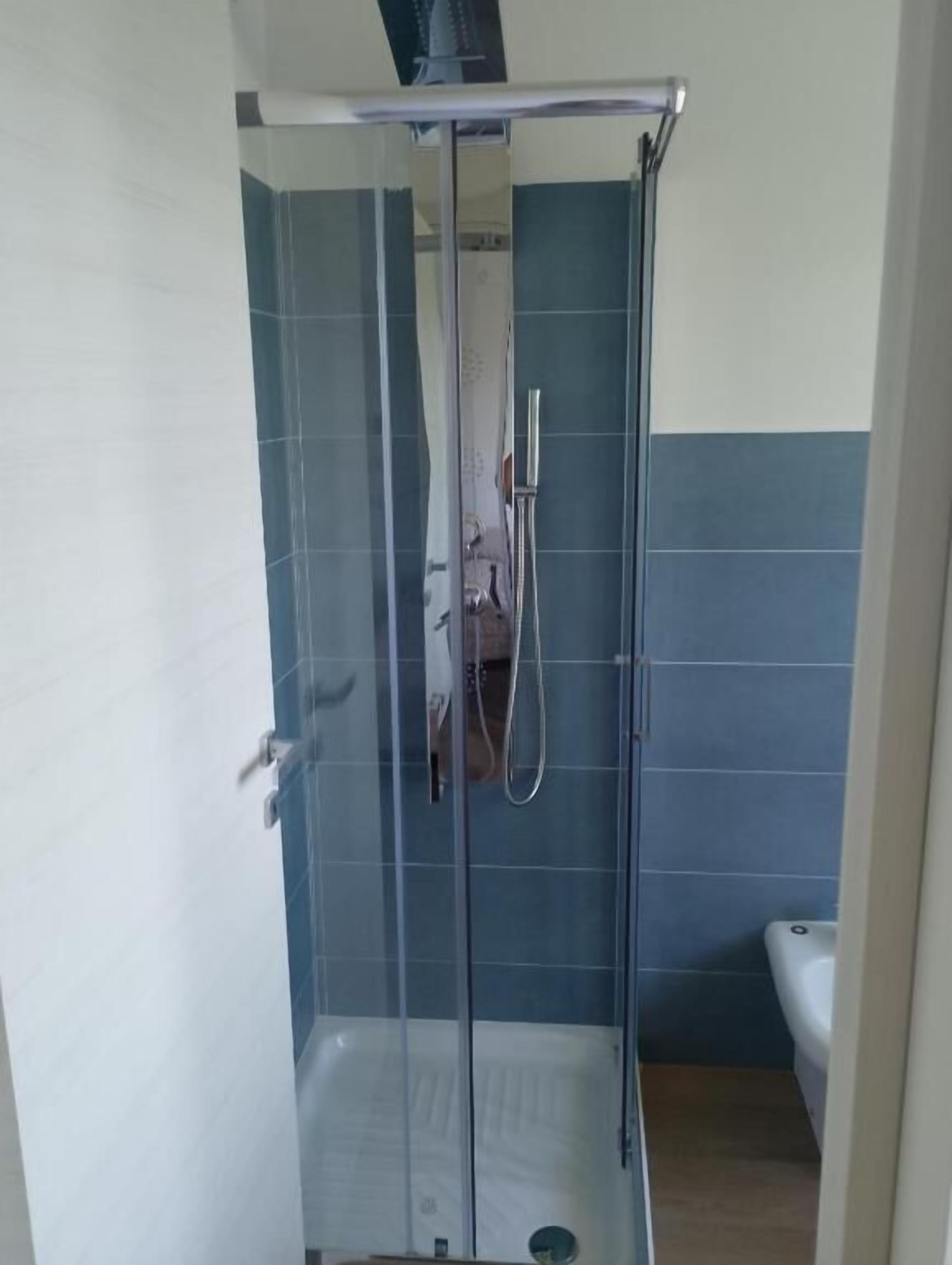 Eine Duschkabine mit Glastür, Handbrause und am Wand montiertem Wasserhahn.