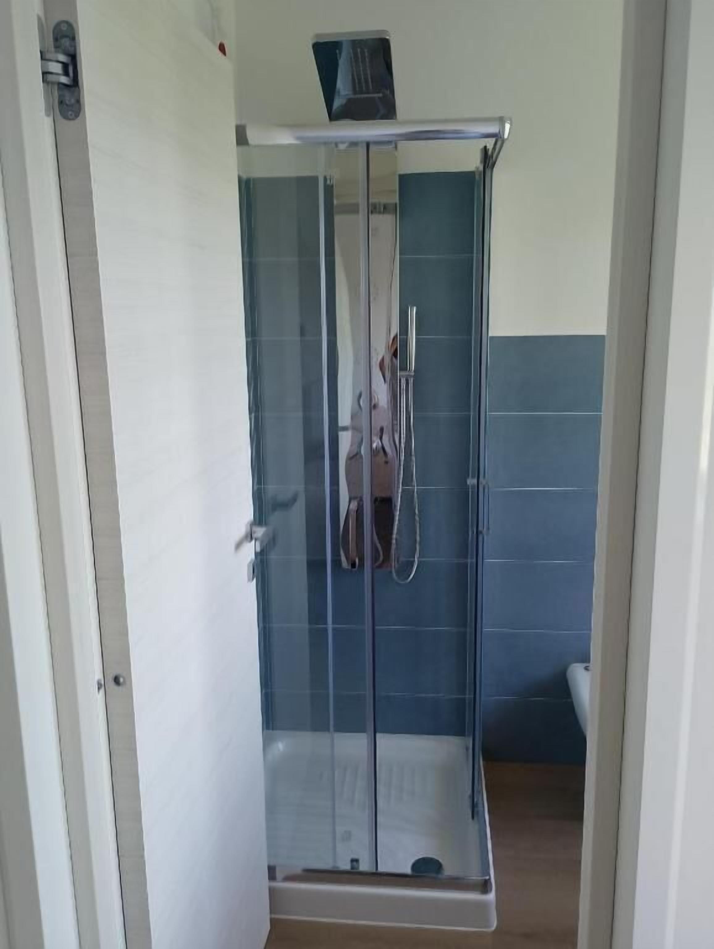 A glass-enclosed shower with a handheld showerhead, a white door, and blue tiled walls.