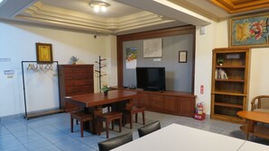 A room with a dining table, chairs, a television, a bookshelf, and a fire extinguisher.